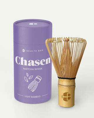 Health Bar Chasen Matcha Besen aus hellem Bambus mit Logo auf dem Griff neben lila Zylinderverpackung mit Aufschrift „Chasen Matcha Whisk Light Bamboo“ vor weißem Hintergrund