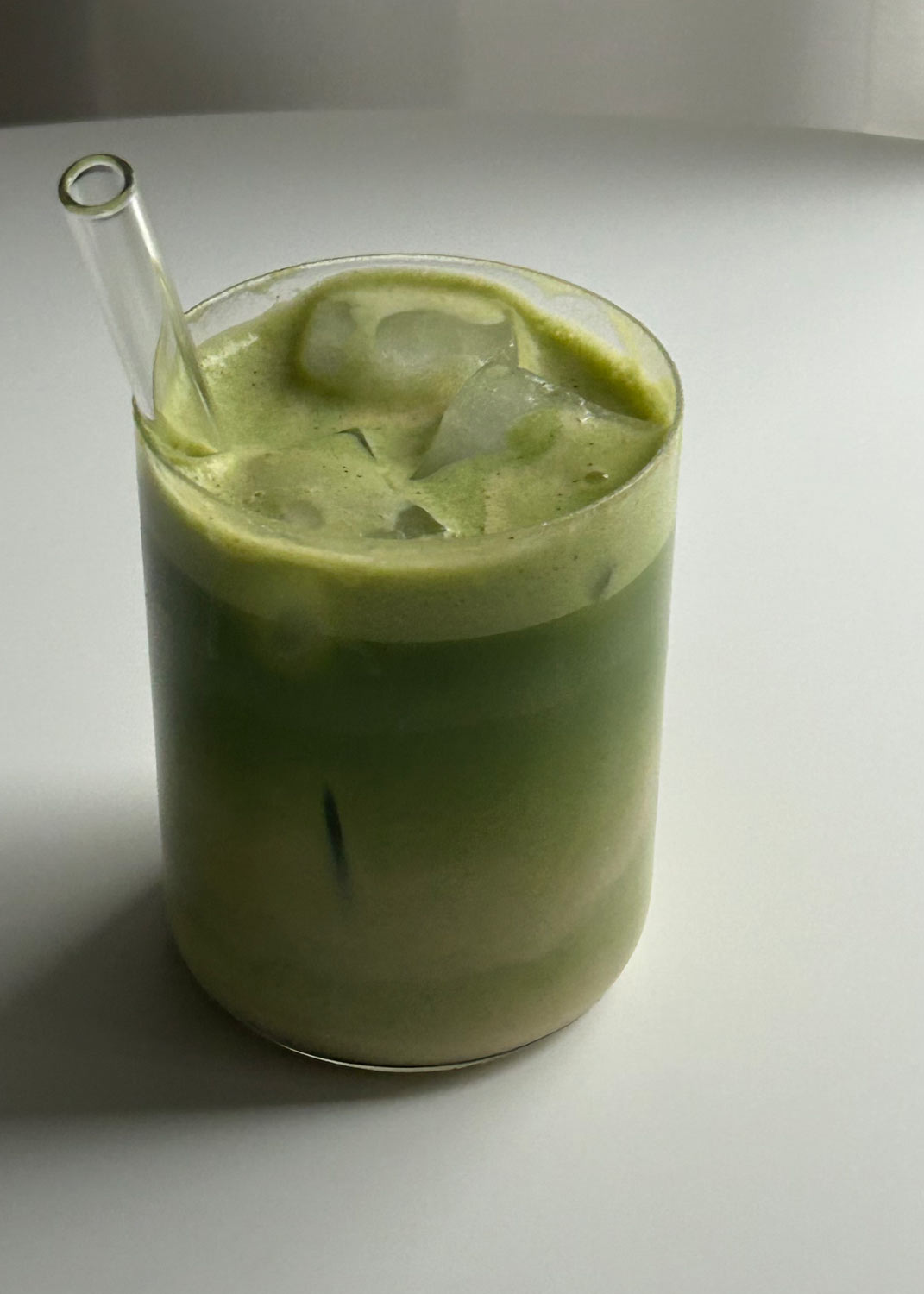 Protein Matcha Latte im Glas mit Eiswürfeln und cremigem grünem Matcha auf weißem Tisch