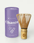 Health Bar Chasen Matcha Besen aus hellem Bambus mit Logo auf dem Griff neben lila Zylinderverpackung mit Aufschrift „Chasen Matcha Whisk Light Bamboo“ vor weißem Hintergrund