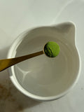 Detailaufnahme von Ceremonial Matcha Pulver im goldenen Löffel über einer weißen Keramikschale