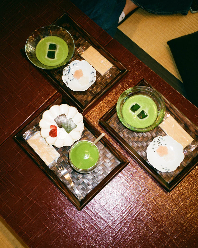 Matcha in Glasschalen und japanische Süßigkeiten auf drei Tabletts, von oben fotografiert