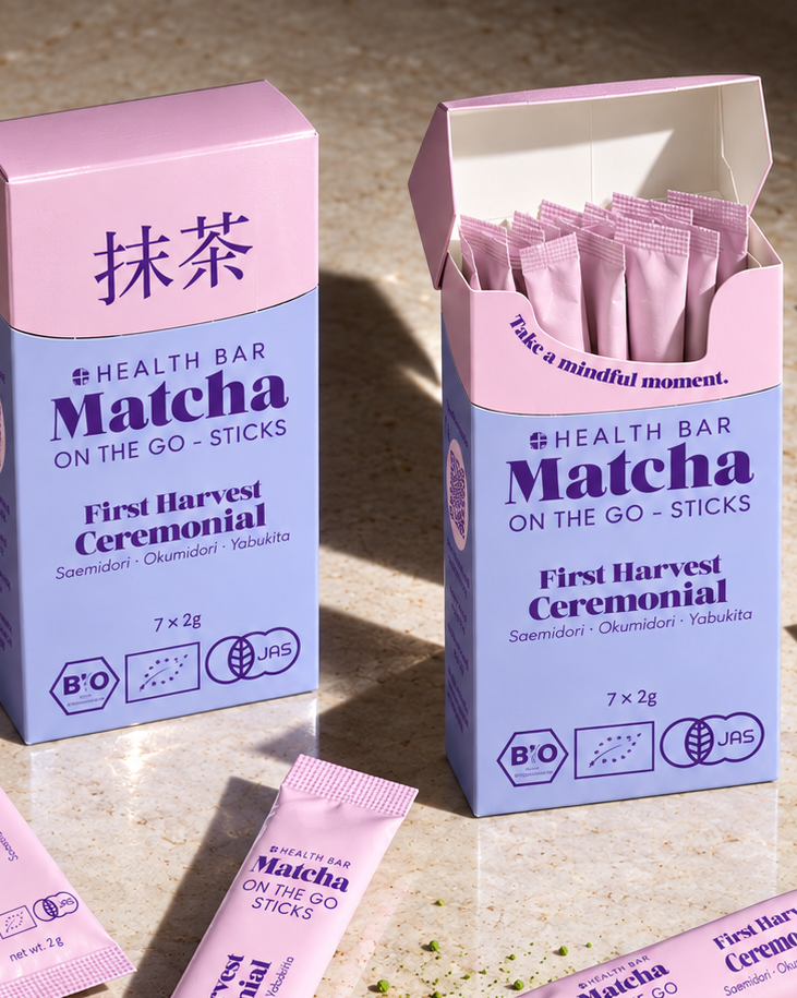 Geöffnete Box Bio Ceremonial Matcha Sticks von Health Bar, daneben ein offener Stick mit Matcha Pulver