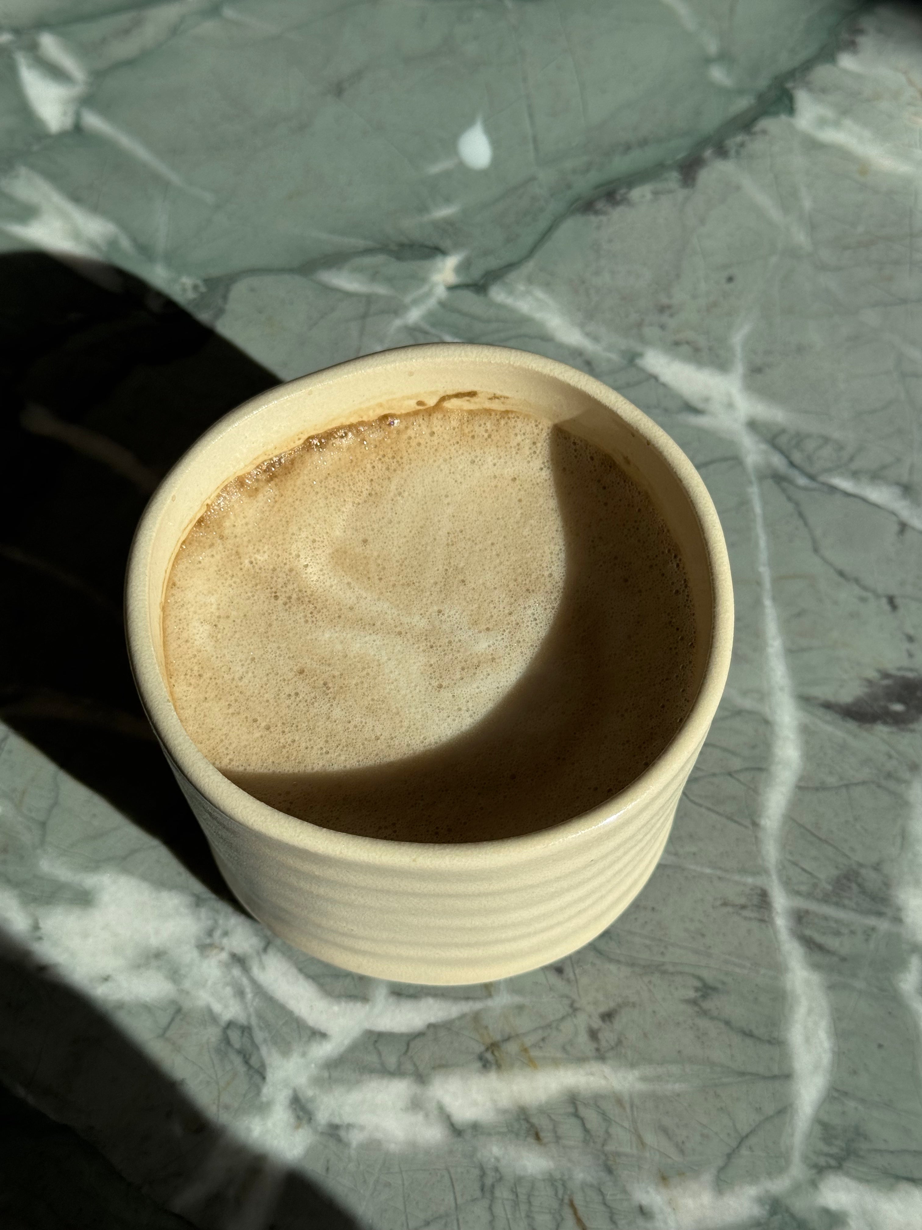 Hojicha Latte in einer Keramikschale mit cremigem Milchschaum auf Marmortisch im Sonnenlicht