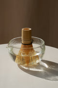 Matcha Besen aus hellem Bambus in transparenter Glas Schale mit Ausguss, warmes Licht und weiche Schatten auf Tisch, Chasen für Matcha Zubereitung und traditionelles Tee Ritual im minimalistischen Setting